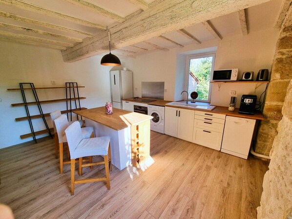 A compact kitchen with wooden flooring, a central island with seating, a washing machine, and a microwave. - Nature View Cottage • Terrace • Piscina (Aguts)