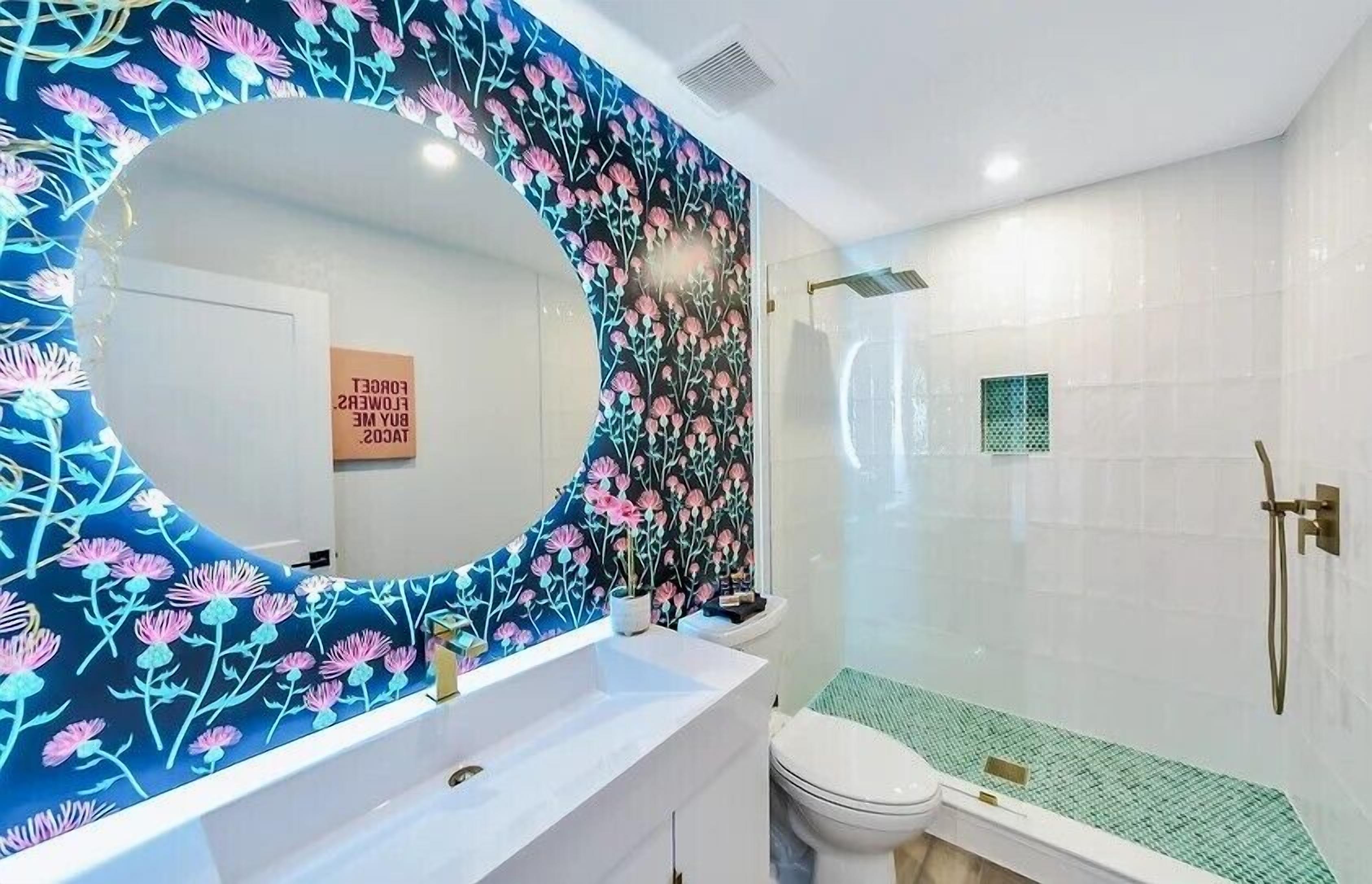 A bathroom with a large mirror, a white sink, a toilet, and a shower area.