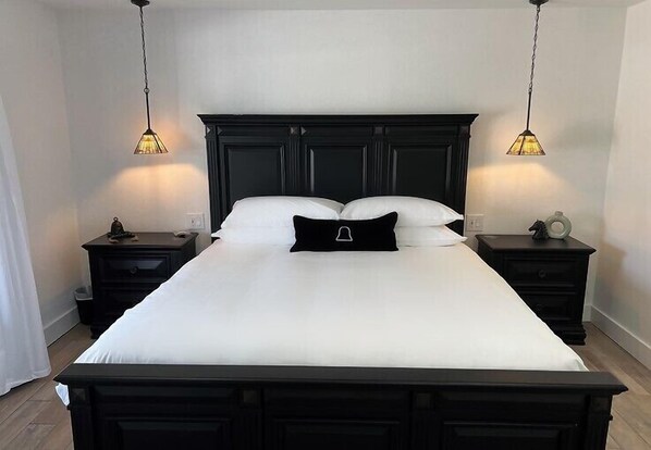 A neatly made bed with a black headboard, two bedside tables with lamps, and a white curtain. - Bell Mare Hotel (Breckenridge)