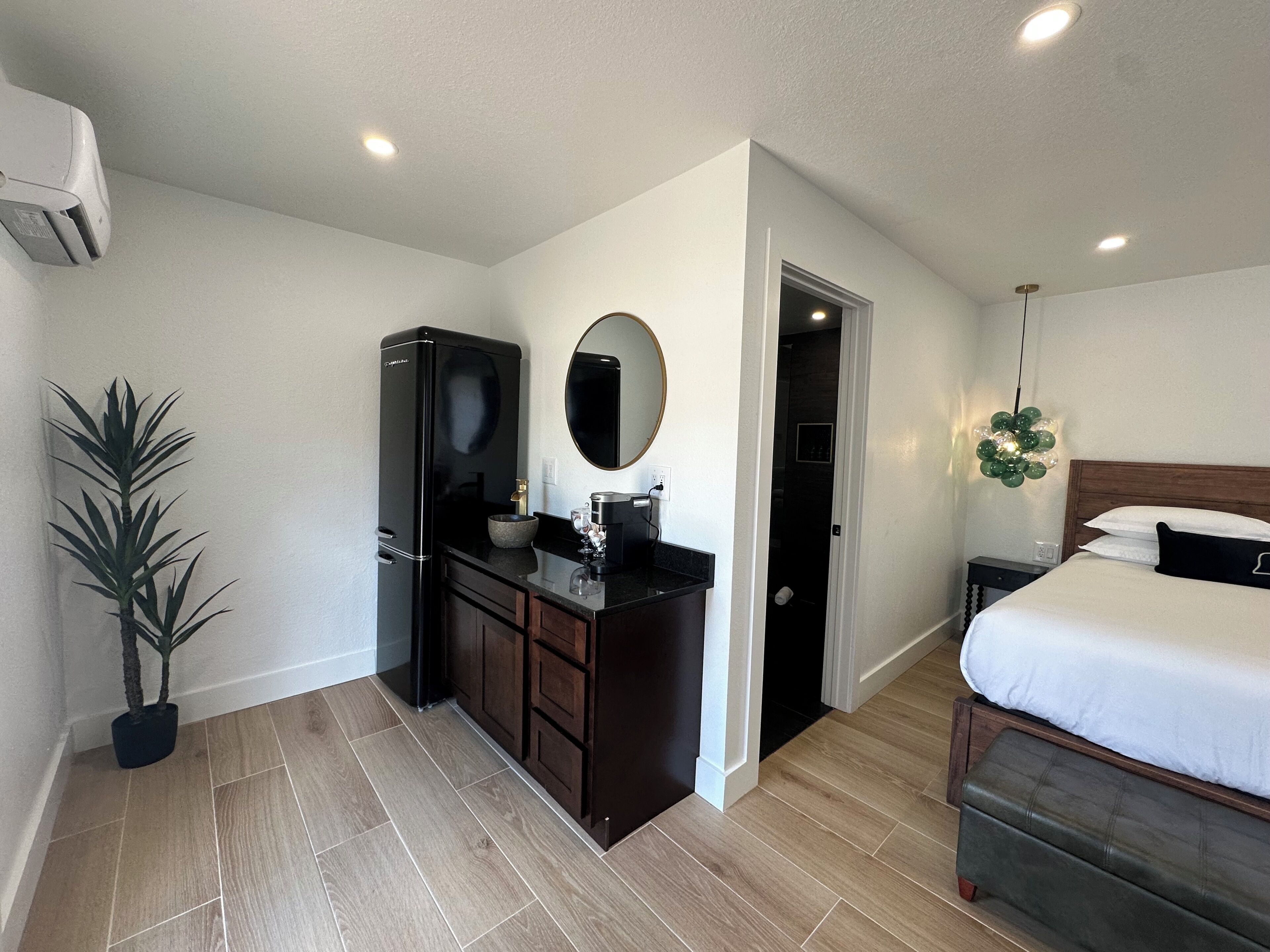 A hotel room with a bed, a dresser, a mirror, a sink, and a potted plant.