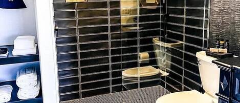 Un baño moderno con paredes de azulejos negros, un inodoro blanco, una zona de ducha y un estante con secadores de pelo.