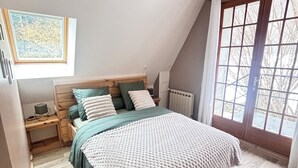 A bedroom with a bed, a desk, a radiator, and a window with a view.