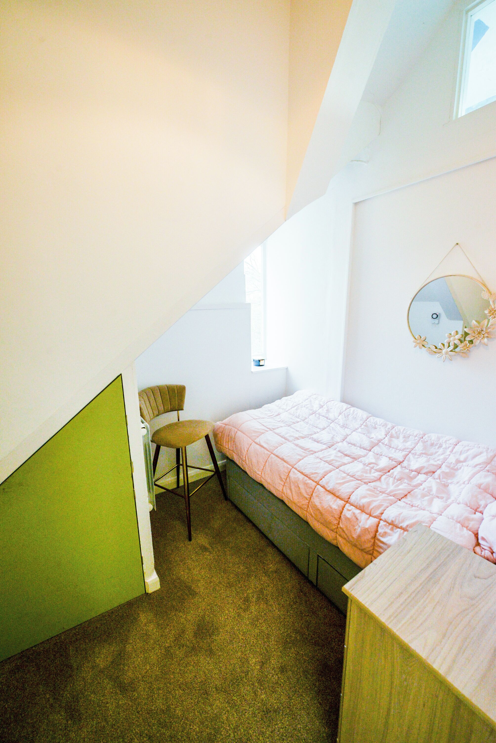 Un dormitorio pequeño y bien iluminado con una cama individual, una silla y un espejo en la pared.
