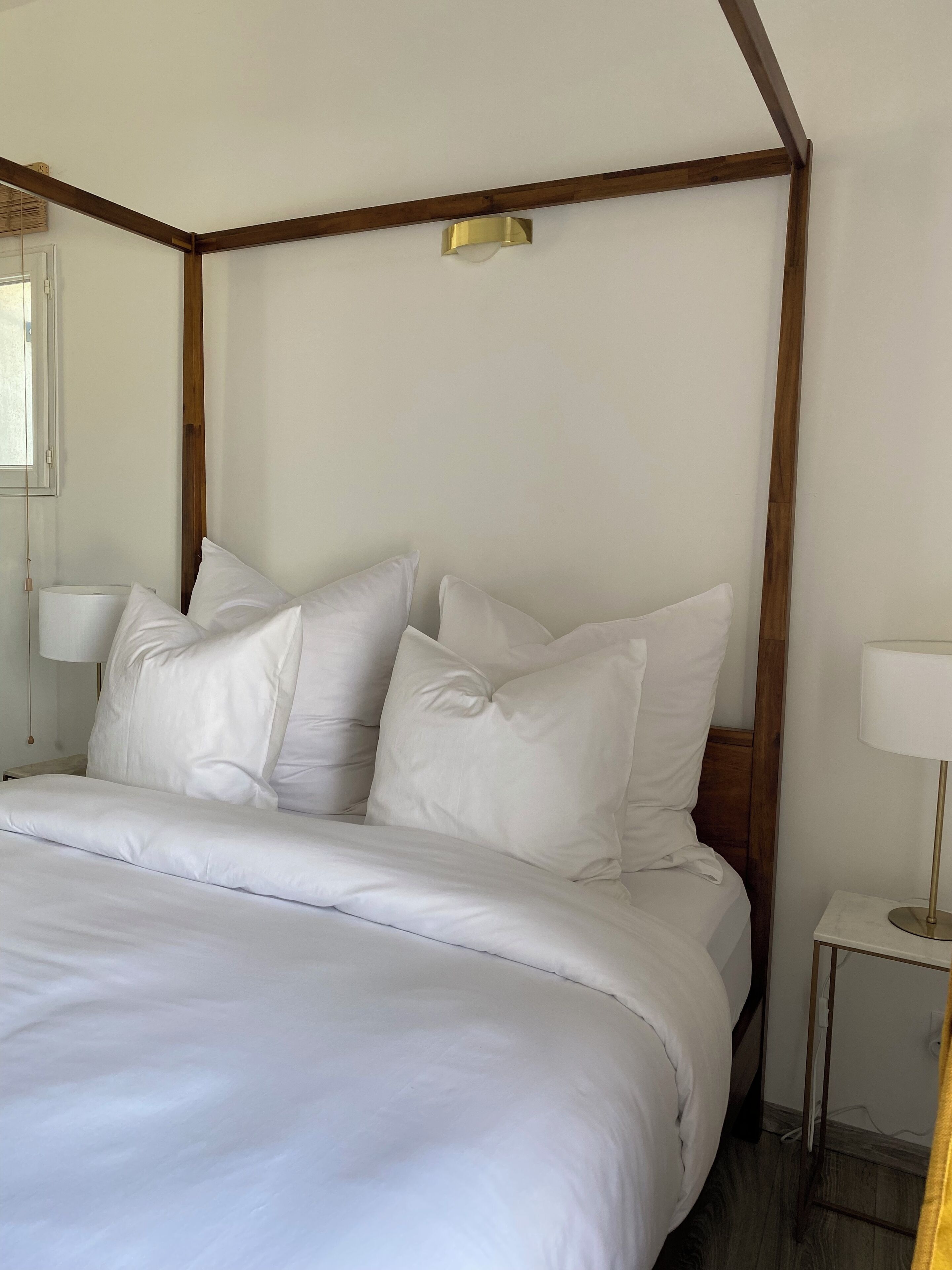 Un lit bien fait, avec du linge de lit blanc et des oreillers, une tête de lit en bois et une table de chevet avec une lampe.