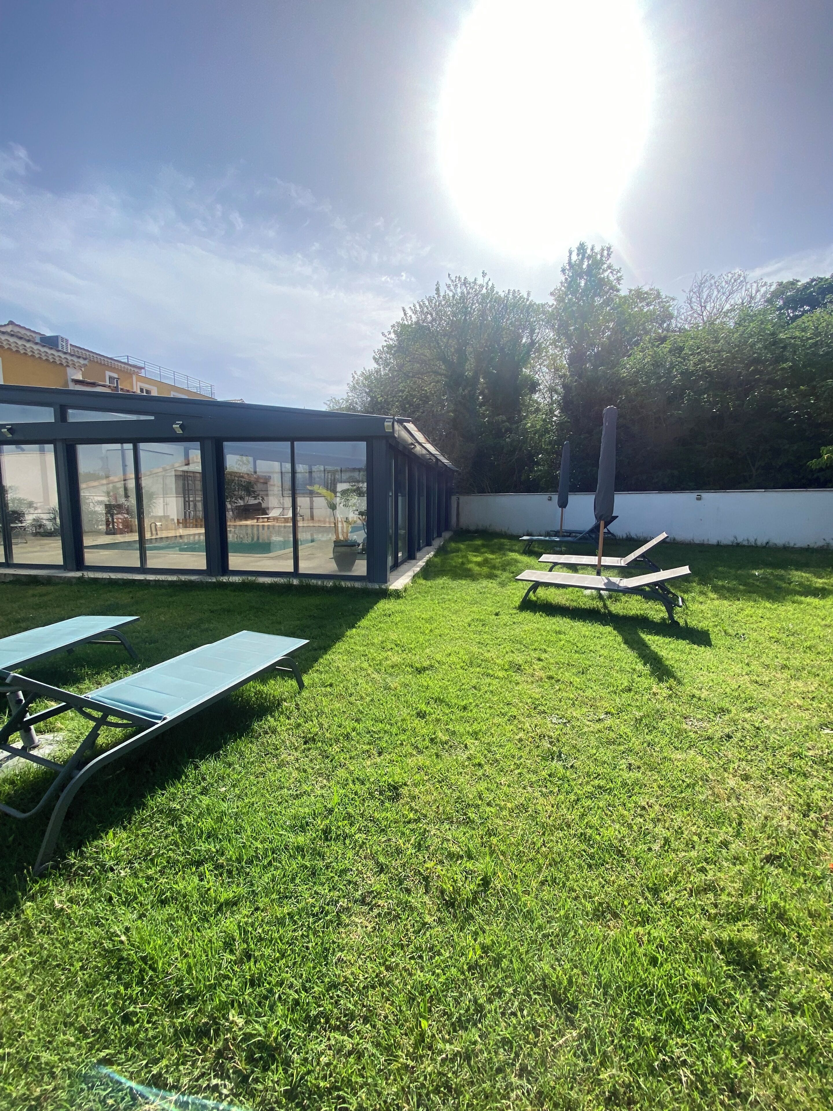 A sunny outdoor area with a glass-enclosed structure, two lounge chairs, and a small table.