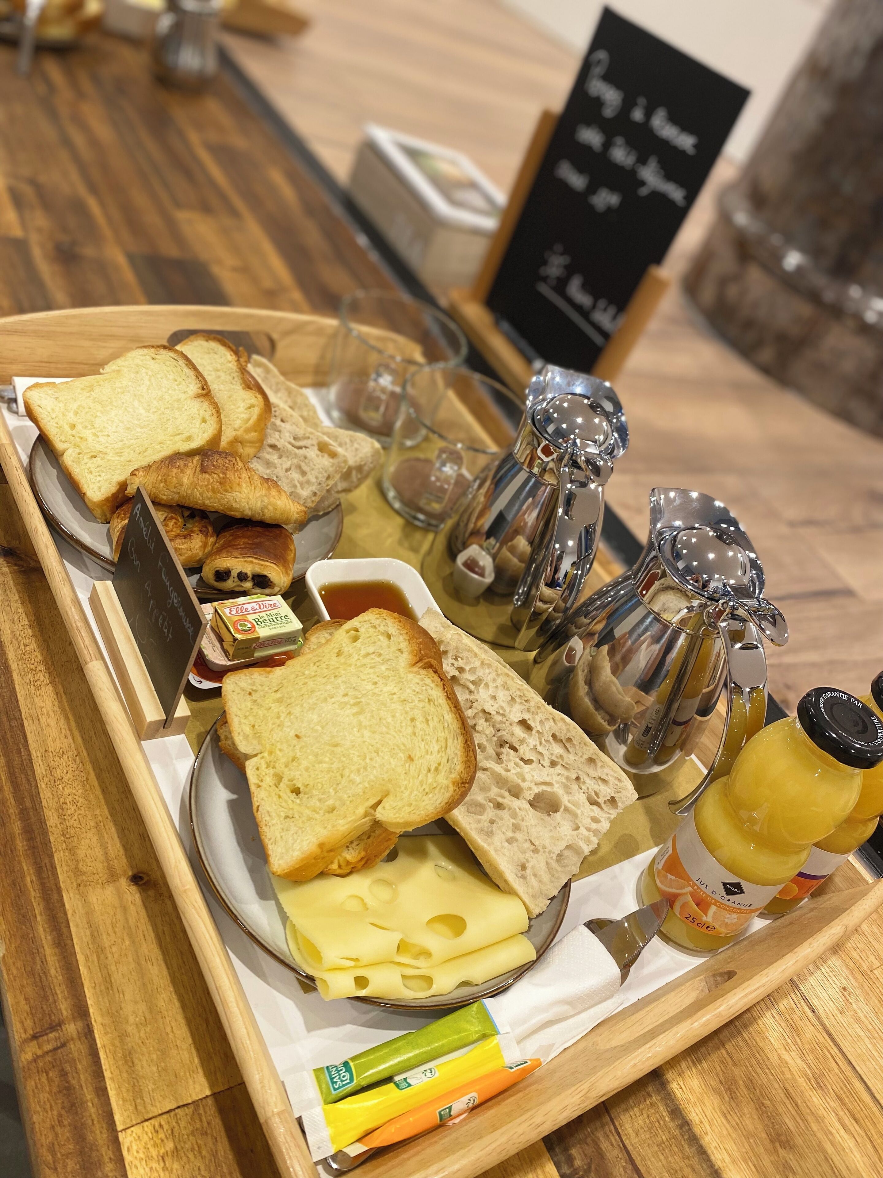 A breakfast tray with bread, croissants, cheese, jam, and condiments.