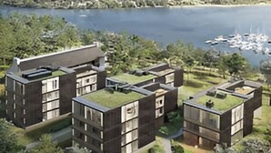 Un moderno complejo de edificios con techos planos, rodeado de vegetación y una masa de agua con barcos.