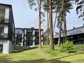 Un bâtiment moderne à plusieurs étages, doté de grandes fenêtres et d’un espace verdoyant avec des arbres.