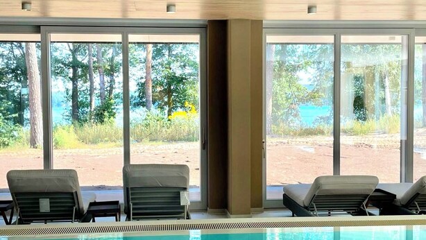 Un área de piscina con dos sillas de descanso y vista a un paisaje natural a través de amplios ventanales.