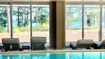 Ett poolområde med två solstolar och utsikt över ett vackert naturlandskap genom stora glasdörrar.
