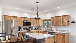 A modern kitchen with wooden cabinets, stainless steel appliances, and a central island with stools. - Charming 2-bedroom Cabin with WiFi, Wood Stove and AC in serene Heber-Overgaard! (Heber-Overgaard)