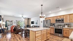 A spacious kitchen with wooden cabinets, a large island, stainless steel appliances, and a dining area with a view of the outdoors. - Charming 2-bedroom Cabin with WiFi, Wood Stove and AC in serene Heber-Overgaard! (Heber-Overgaard)