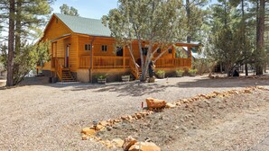 A wooden cabin with a porch, surrounded by trees and a gravel driveway. - Charming 2-bedroom Cabin with WiFi, Wood Stove and AC in serene Heber-Overgaard! (Heber-Overgaard)