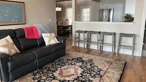 A living room with a black leather sofa, a patterned rug, and a dining area with a table and chairs. - Charming Beachfront 4-bedroom cottage with WiFi, AC in Coldwater (Coldwater)