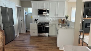A modern kitchen with white cabinetry, stainless steel appliances, and a wooden floor. - Charming Beachfront 4-bedroom cottage with WiFi, AC in Coldwater (Coldwater)