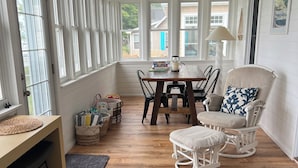 A sunlit room with a dining table, chairs, a rocking chair, and a ceiling fan. - Charming Beachfront 4-bedroom cottage with WiFi, AC in Coldwater (Coldwater)
