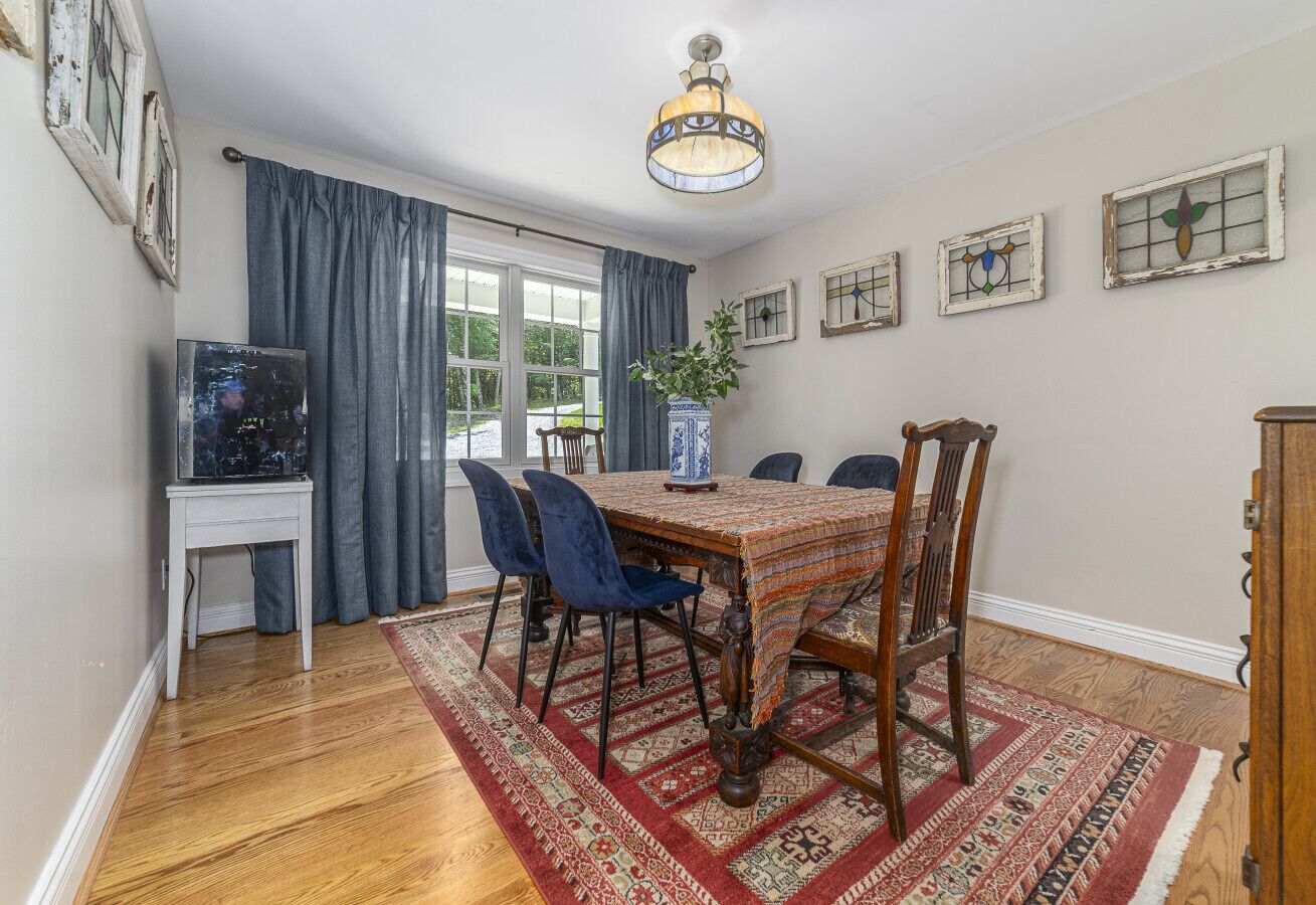 A dining area with a wooden table, blue chairs, a patterned rug, and a television on a stand.