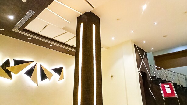 A modern hotel lobby with a central pillar, geometric wall art, and a staircase. - HOTEL GK PALACE (East Jorhat)