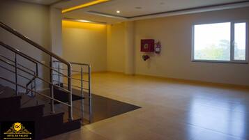 Interior de un hotel con una escalera, un extintor y un ventanal grande.