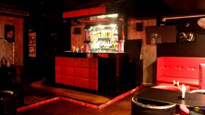 A bar area with a red cushioned seating area and a bar counter displaying various bottles. - HOTEL GK PALACE (East Jorhat)