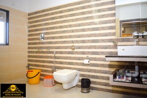 A bathroom with striped tile walls, a toilet, a sink, and a bucket. - HOTEL GK PALACE (East Jorhat)