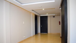 A hotel corridor with a tiled floor, a ceiling light, and a black door at the end. - HOTEL GK PALACE (East Jorhat)