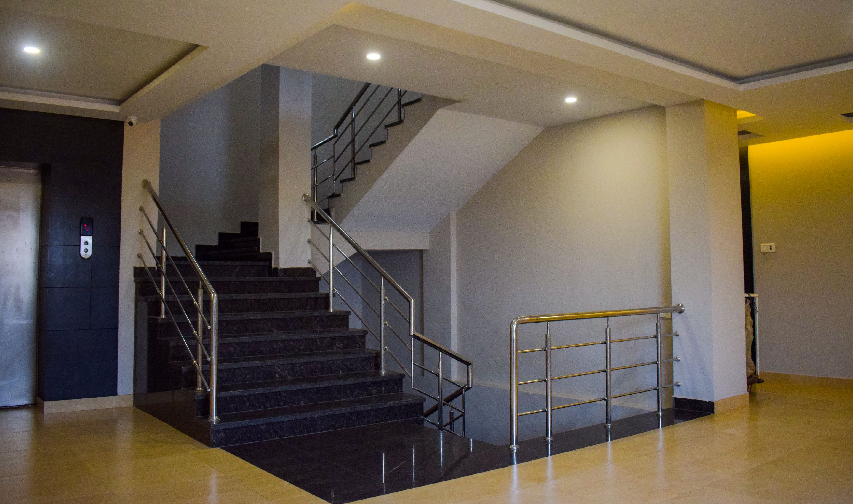 Interior moderno de hotel con escalera, barandilla y botón de ascensor.