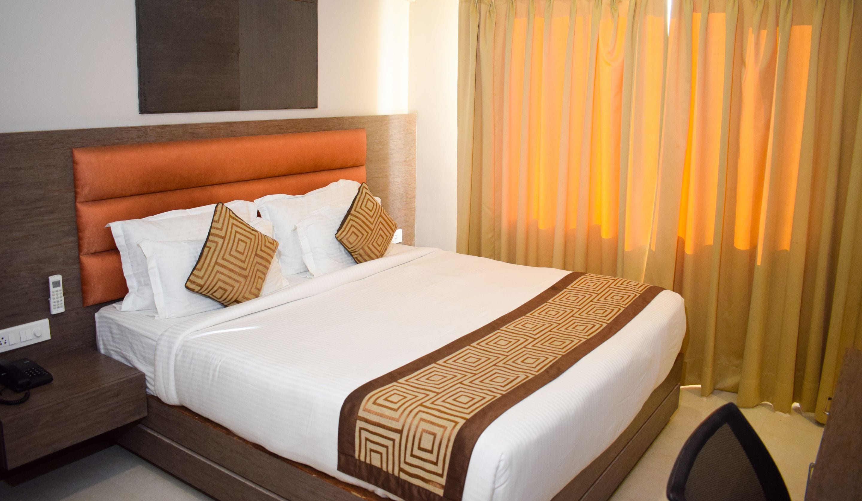 A hotel room with a large bed, a wooden headboard, a bedside table with a phone, and a window with curtains.