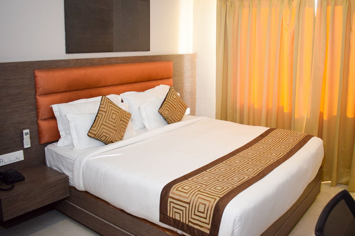 A hotel room with a large bed, a wooden headboard, a bedside table with a phone, and a window with curtains.