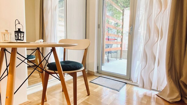 Ein Zimmer mit Holzboden, einem Esstisch mit Stühlen, einer Schiebeglastür und Blick ins Freie.