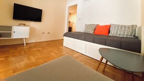 Ein modernes Wohnzimmer mit Sofa, Fernseher, kleinem Tisch und Holzboden.