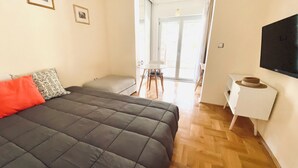 Ein Schlafzimmer mit einem großen Bett, einem kleinen Tisch, einem Fernseher und Blick ins Freie.