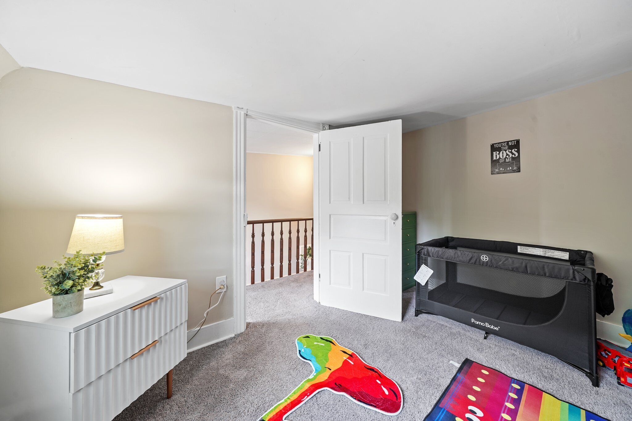 Habitació infantil amb un llit superposat, un calaix blanc, una làmpada i un joguet colorit a terra.