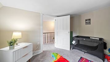 Habitació infantil amb un llit superposat, un calaix blanc, una làmpada i un joguet colorit a terra.