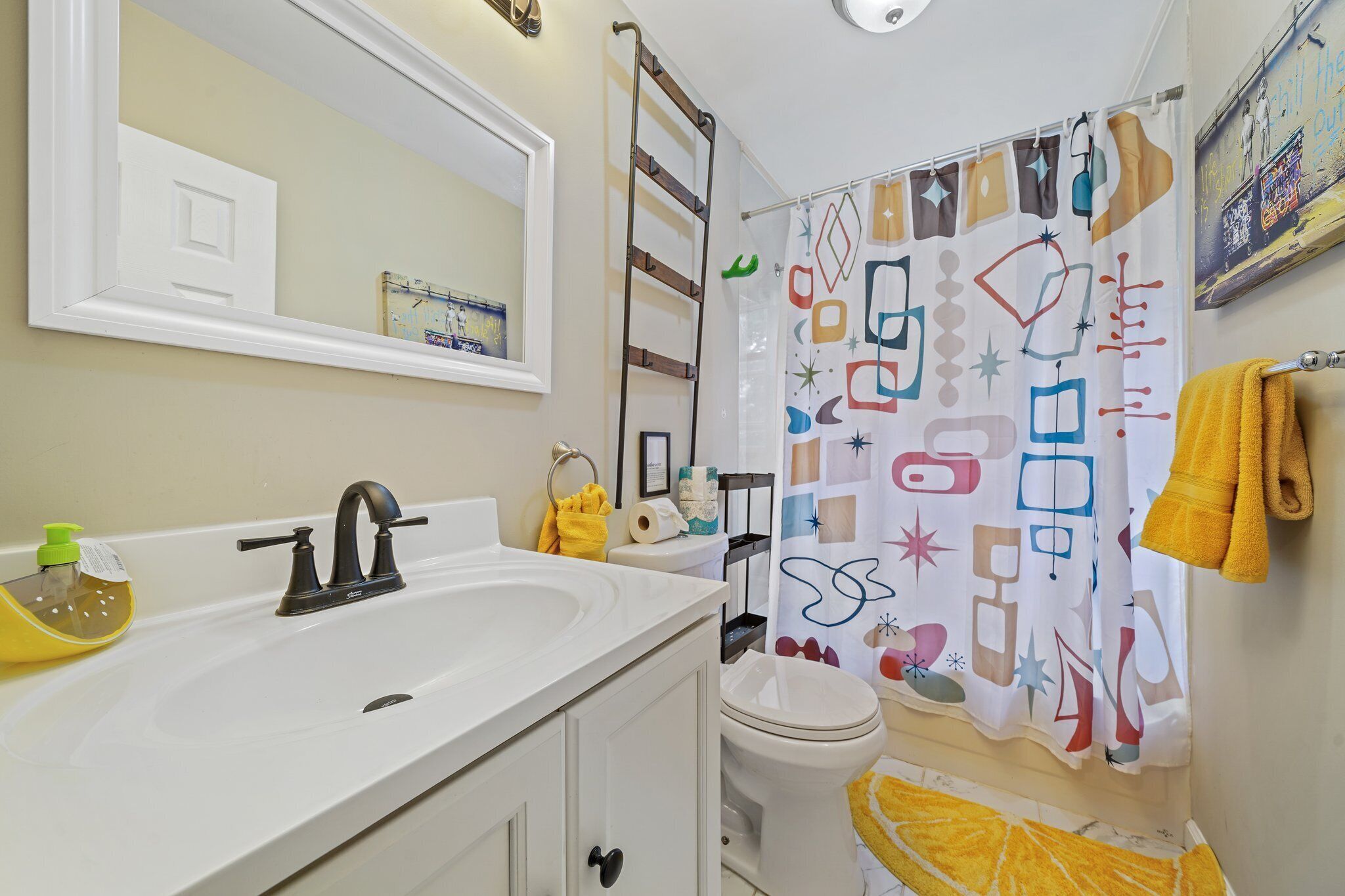 A bathroom with a white sink, a mirror, a toilet, and a shower curtain with abstract patterns.