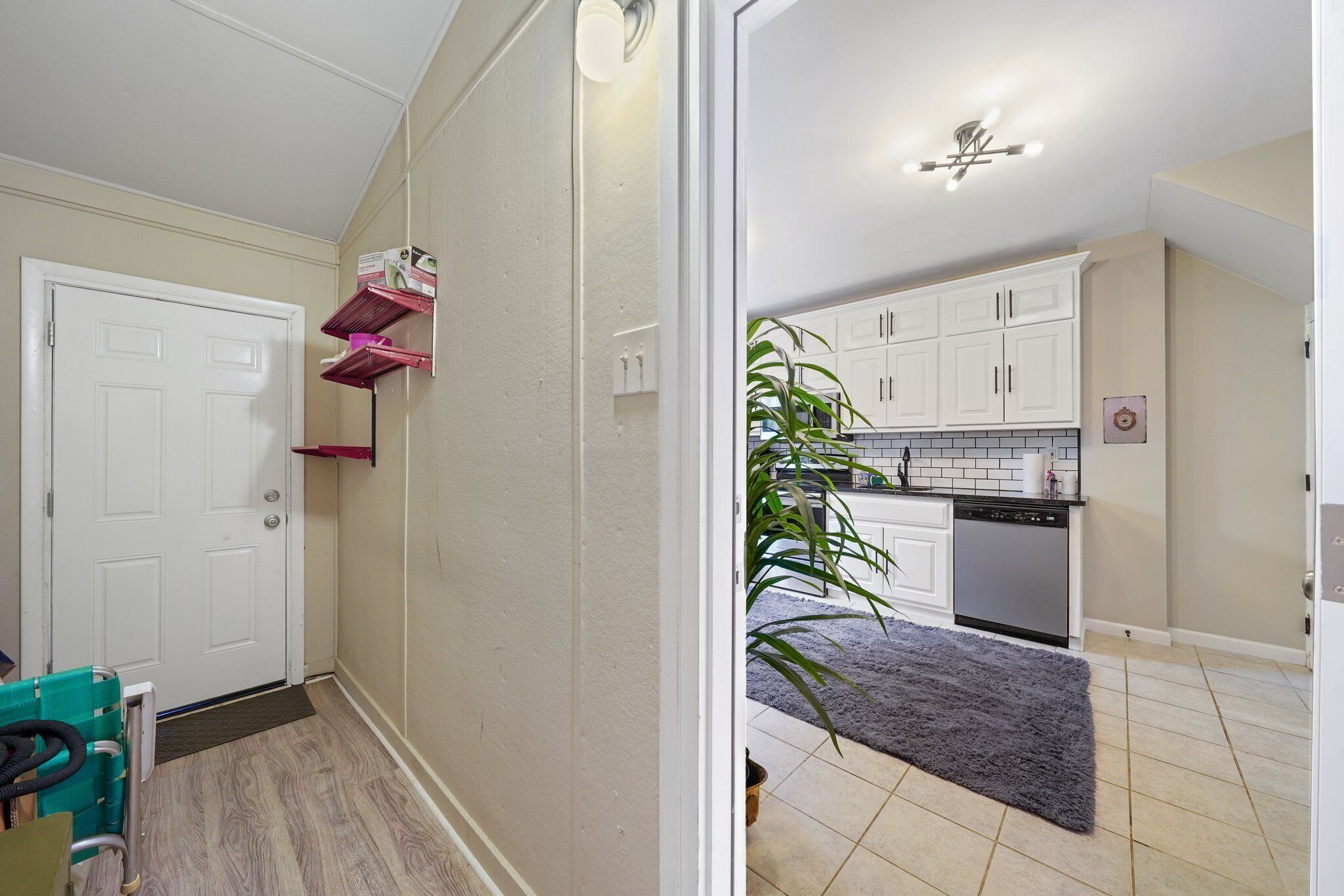 A hallway leading to a kitchen with white cabinets, a dishwasher, and a potted plant.