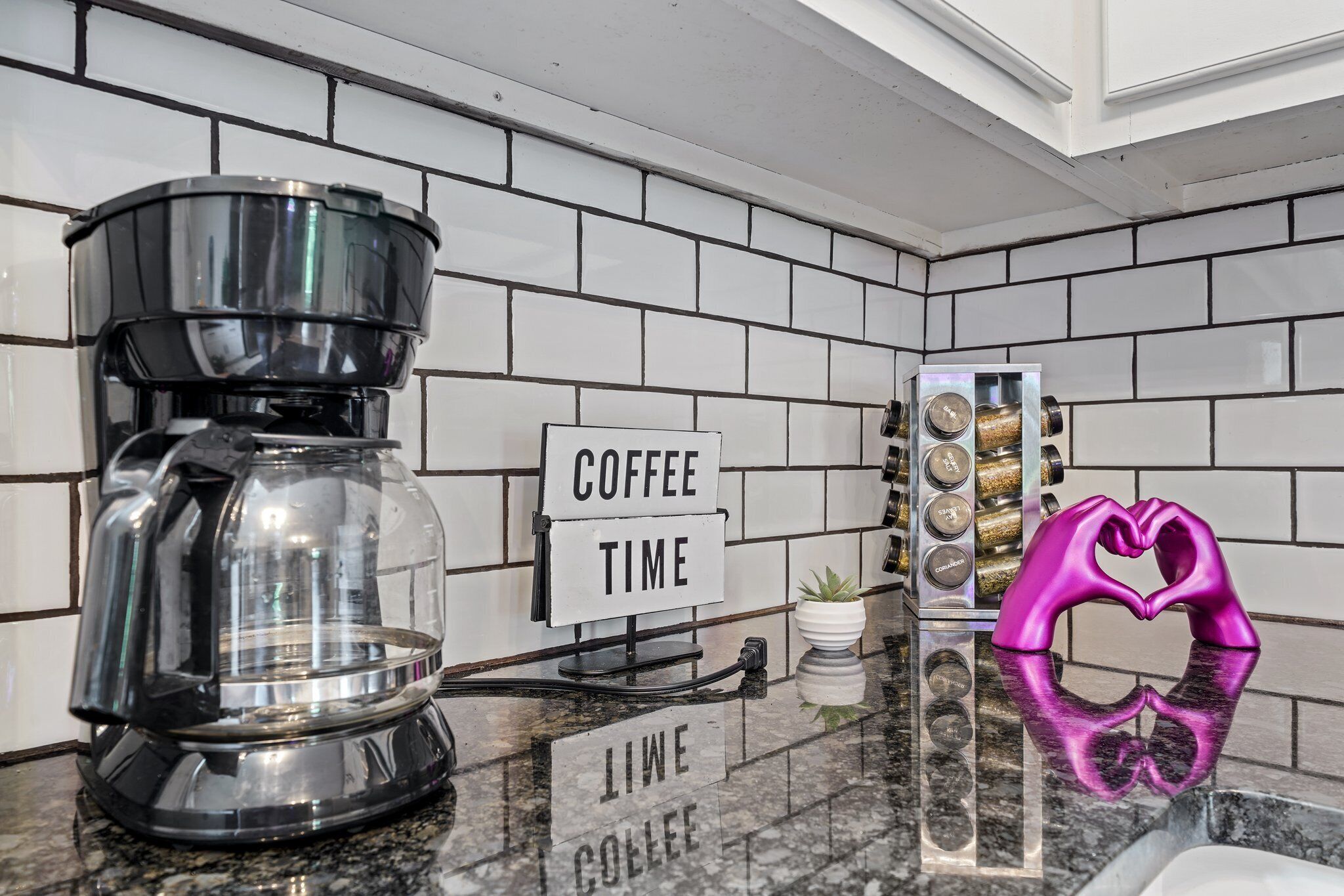 Une cuisine équipée d’une machine à café, d’une pancarte indiquant « PAUSE CAFÉ » et d’un objet décoratif en forme de cœur posé sur le comptoir.
