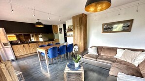 Ein modernes Wohnzimmer mit einem Holztisch, blauen Sesseln, einem braunen Sofa und einer Küche im Hintergrund.