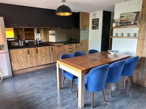 Eine moderne Küche mit dunklen Schränken, einem Holztisch und blauen Stühlen.