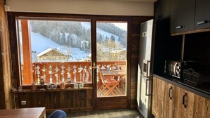 Eine Küche mit Holzausstattung, ein Essbereich mit Tisch und Stühlen und Blick auf eine verschneite Landschaft durch ein großes Fenster.