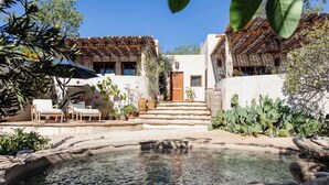 Un pati amb una piscina, zones d'estar a l'exterior i una escala que condueix a un edifici amb una porta de fusta.