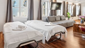 Ett hotellrum med två sängar, en soffa, en TV och ett trägolv.