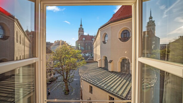 En utsikt från ett fönster med utsikt över en gata med byggnader, inklusive en kyrka med ett högt torn.