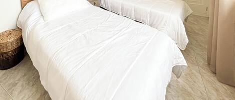Two single beds with wooden headboards, a wicker basket, and a tiled floor.