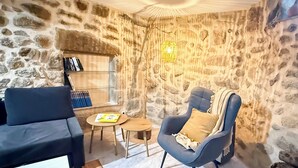 Habitació acollidora amb una paret de pedra, un butaques blau, un sofà negre i una taula de fusta petita amb llibres.