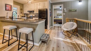 A kitchen with a central island, bar stools, a dog bowl, and a wooden railing. - Pet-Friendly Creekside Cabin w/ Hot Tub 2BR/2 Bath (Ellijay)