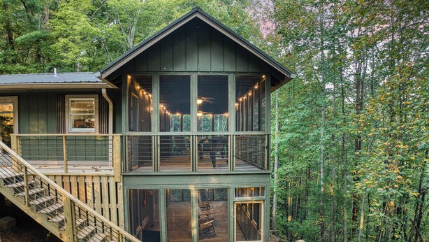 A two-story wooden cabin with a balcony and a deck, surrounded by dense forest. - Pet-Friendly Creekside Cabin w/ Hot Tub 2BR/2 Bath (Ellijay)