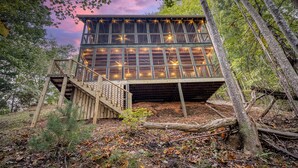 A wooden cabin with a balcony, surrounded by trees and a forest floor covered with leaves. - Pet-Friendly Creekside Cabin w/ Hot Tub 2BR/2 Bath (Ellijay)