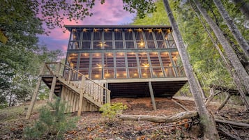 Une cabane en bois dotée d’un balcon, entourée d’arbres et bordée d’un tapis de feuilles.