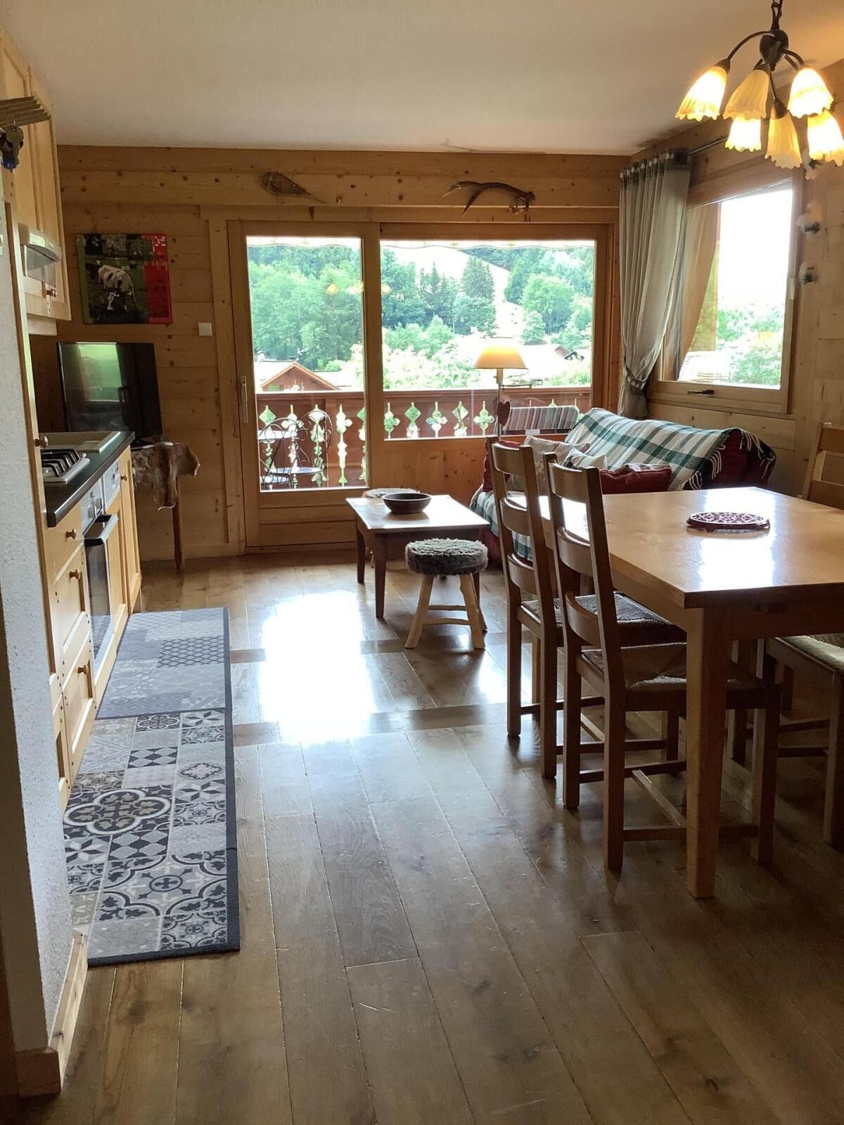 Interior acogedor de una cabaña con una mesa de comedor de madera, sillas, una pequeña cocina y un ventanal con vistas al exterior.